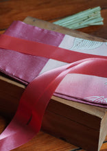 Load image into Gallery viewer, Ravissante ceinture de style obi, cet accessoire tendance, pièce incontournable de la garde-robe met la taille en valeur et affine la silhouette. Les côtés sont en soie, le tissu central de kimono qui représente des fleurs blanches est rose thé et le ruban rose saumon.

