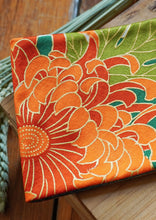 Load image into Gallery viewer, Ravissante ceinture de style obi, cet accessoire tendance, pièce incontournable de la garde-robe met la taille en valeur et affine la silhouette. Les côtés sont orange brulé, le tissu central de kimono représente une belle fleur de chrysanthème orange. Le ruban est orange vif.
