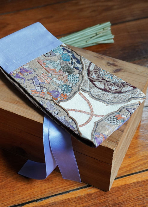 Ravissante ceinture de style obi, cet accessoire tendance, pièce incontournable de la garde-robe met la taille en valeur et affine la silhouette. Les côtés sont parme et le motif central représente une scène avec des personnages de cour dans les tons violets, marron et doré.