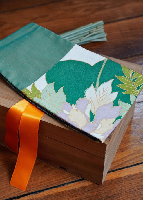 Ravissante ceinture de style obi, cet accessoire tendance, pièce incontournable de la garde-robe met la taille en valeur et affine la silhouette.  Les côtés sont vert jade, le tissu central est un kimono en soie avec des fleurs mauves, des glycines et des feuilles. Le ruban est orange mandarine.